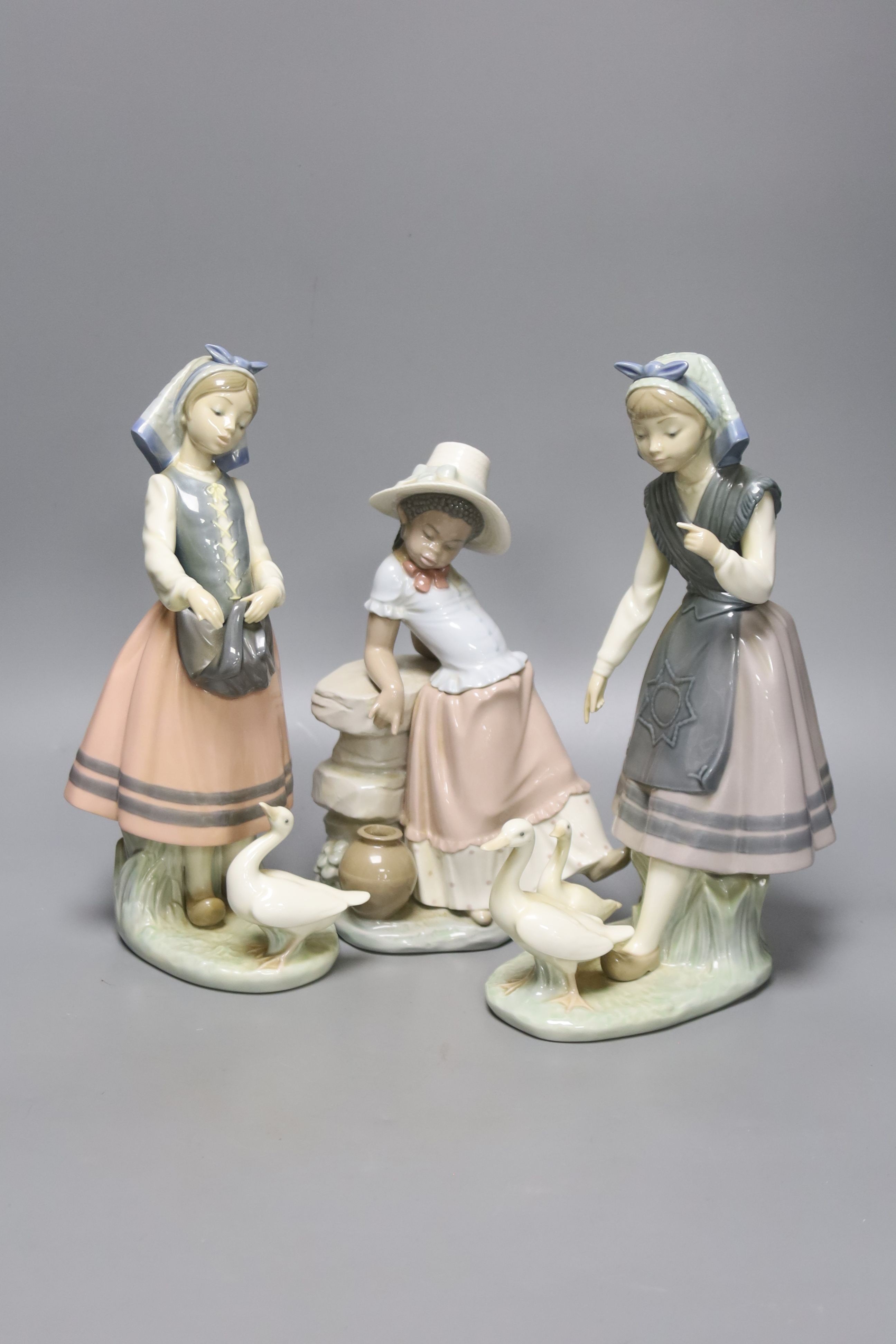 A Lladro figure of a girl feeding a duck, another sitting on a wall, and a girl with two ducks, tallest 26cm